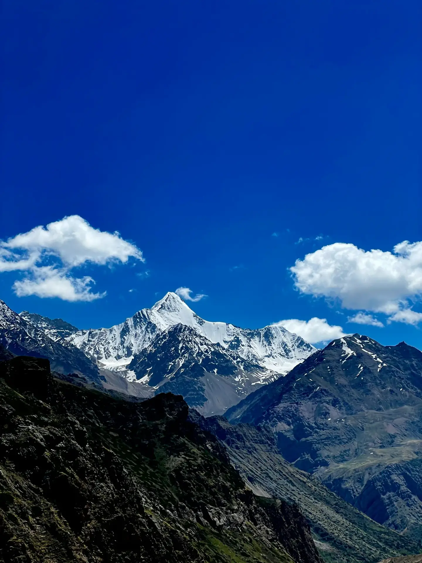 Snowy mountain range under a clear blue sky with a few clouds on the horizon.